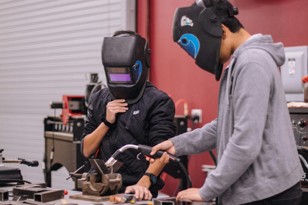 Two welders in protective gear concentrate on a project in a workshop setting.